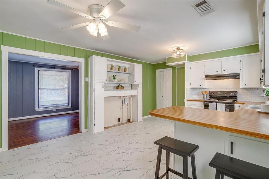 Kitchen featuring decorative backsplash, electric range, a kitchen breakfast bar, white cabinetry, and light wood-type flooring