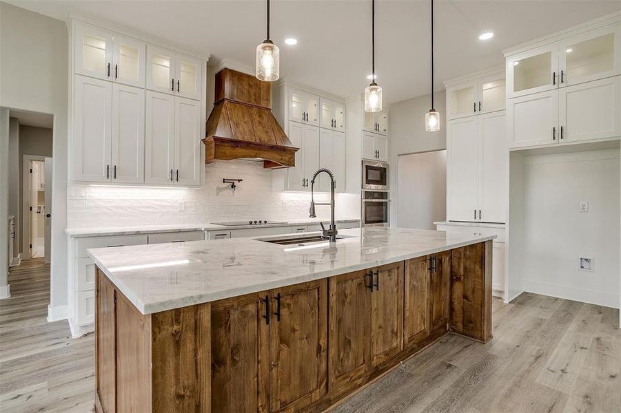 Kitchen with white cabinets, an island with sink, and premium range hood