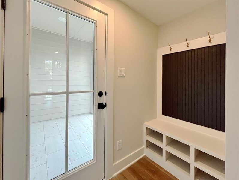 Welcome into an inviting entryway, featuring a sleek built-in bench with convenient storage, complemented by modern hooks for a tidy organization, all basking in the natural light streaming through a full-length glass door.