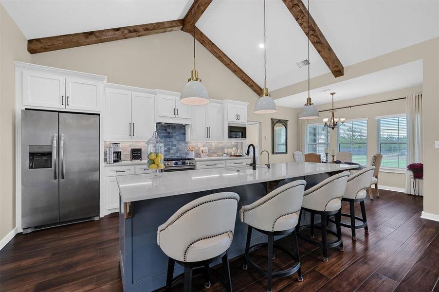 Kitchen with a kitchen island with sink, beam ceiling, dark wood-type flooring, stainless steel appliances, and pendant lighting