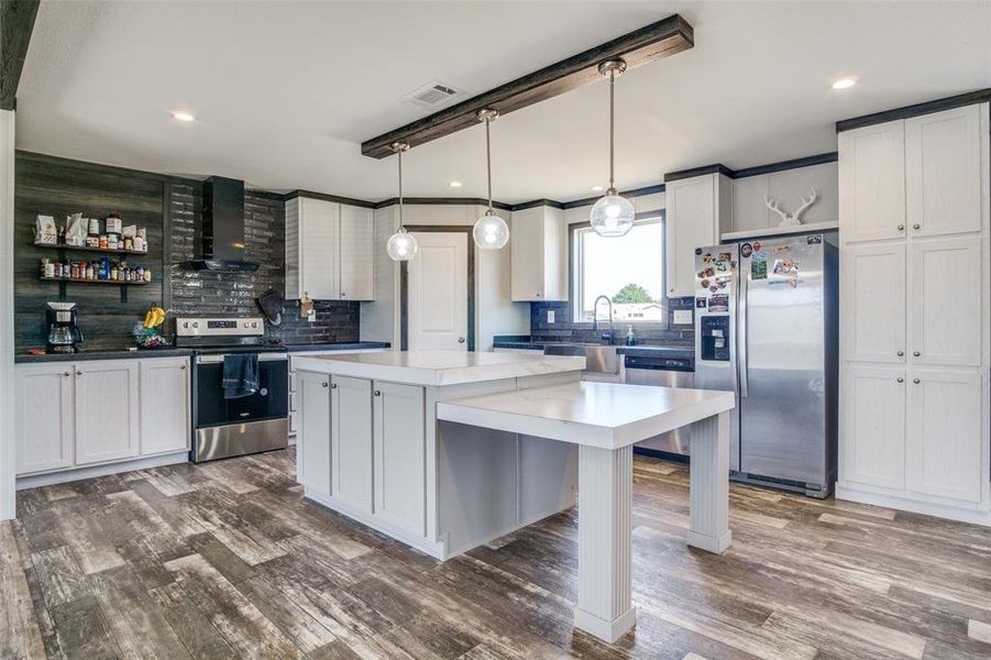 Kitchen with appliances with stainless steel finishes, decorative backsplash, a center island, decorative light fixtures, and wall chimney range hood