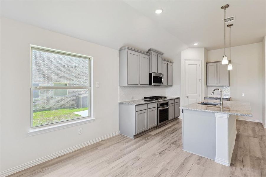 Kitchen with pendant lighting, sink, vaulted ceiling, light hardwood / wood-style flooring, and appliances with stainless steel finishes