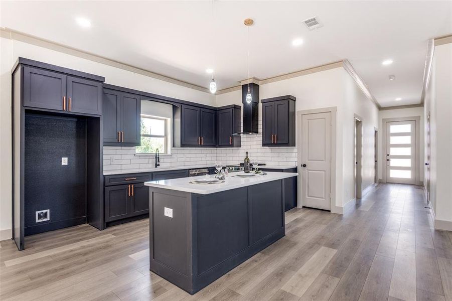 Kitchen featuring light hardwood / wood-style floors, crown molding, backsplash, and wall chimney exhaust hood