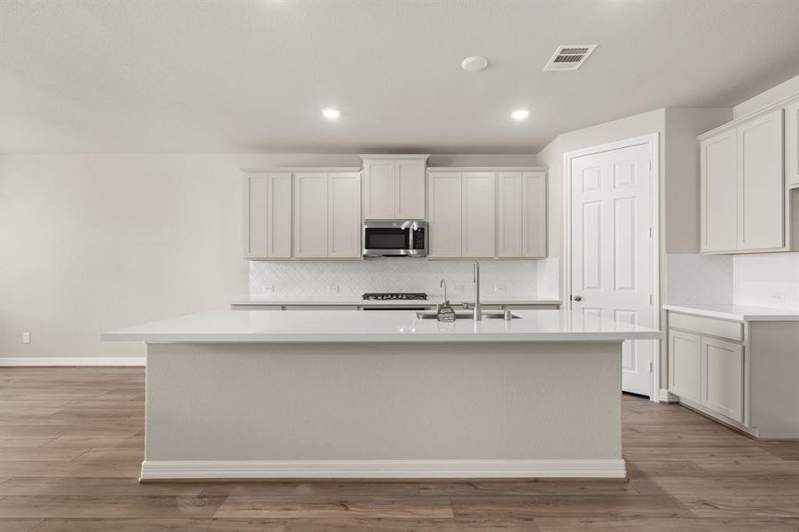 This light and bright kitchen features a large quartz island, white cabinets, a large sink overlooking your family room, recessed lighting, and beautiful backsplash.