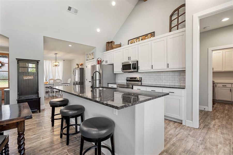 Kitchen with white cabinets, an island with sink, light hardwood / wood-style flooring, stainless steel appliances, and a breakfast bar area