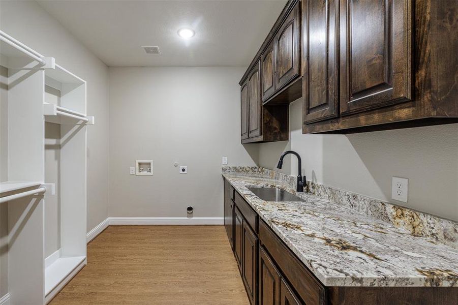 Clothes washing area with light hardwood / wood-style floors, washer hookup, electric dryer hookup, cabinets, and sink