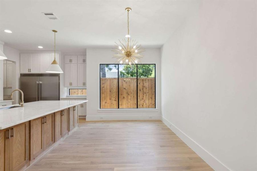 Kitchen with white cabinets, stainless steel built in refrigerator, pendant lighting, light wood-type flooring, and an inviting chandelier