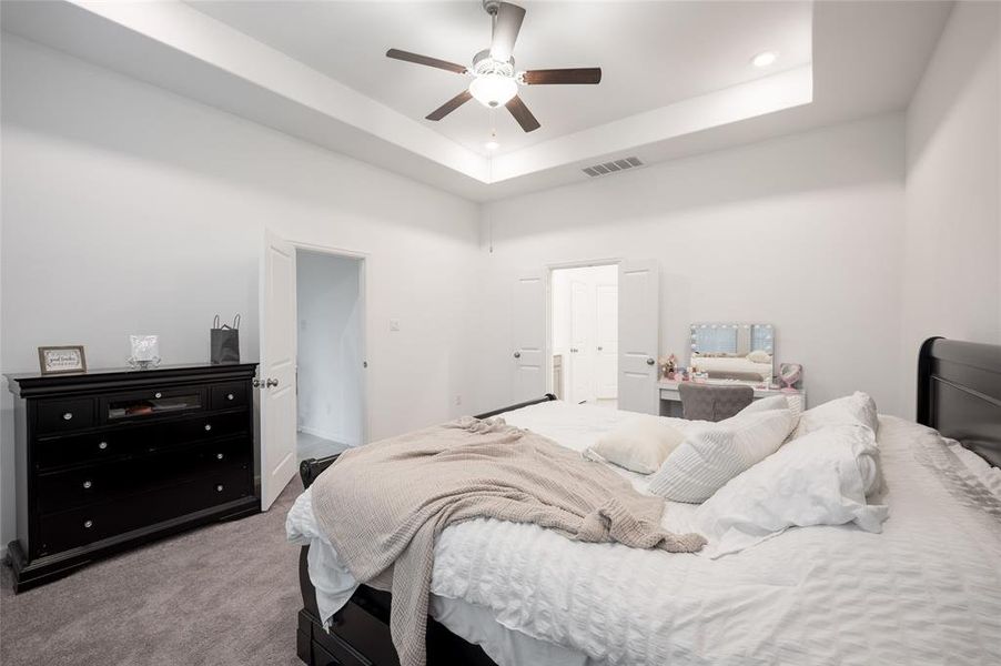 Tray ceilings take center stage in this stunning primary bedroom. Natural light pours through the large windows, creating a bight and airy atmosphere.