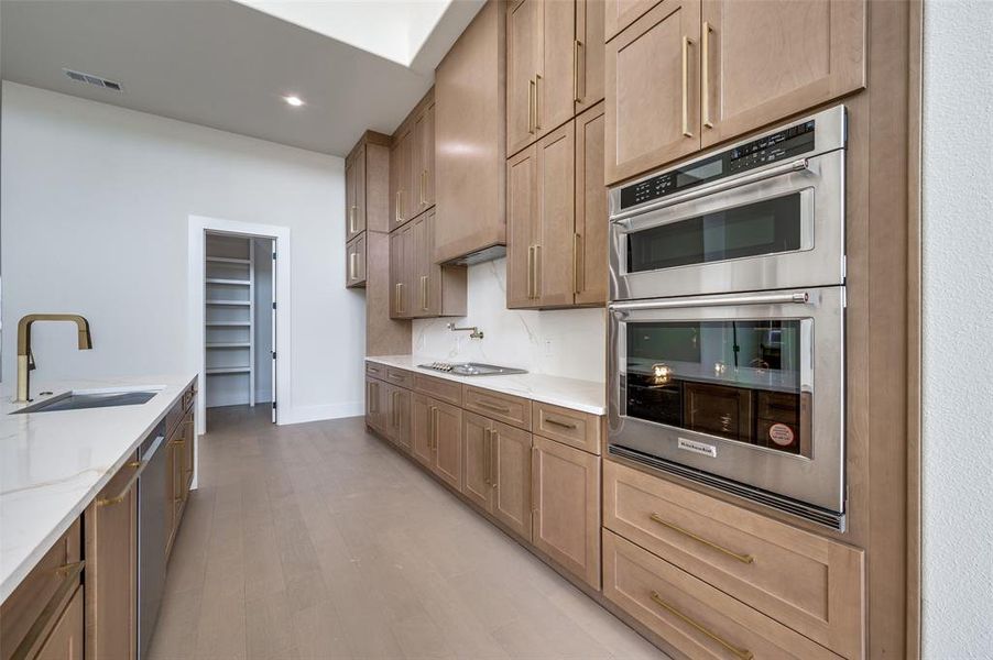 Kitchen with stainless steel double oven, white cooktop, light hardwood / wood-style flooring, sink, and light stone counters