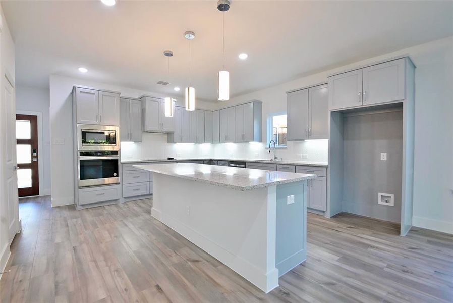 Kitchen with appliances with stainless steel finishes, hanging light fixtures, light hardwood / wood-style floors, gray cabinetry, and a center island