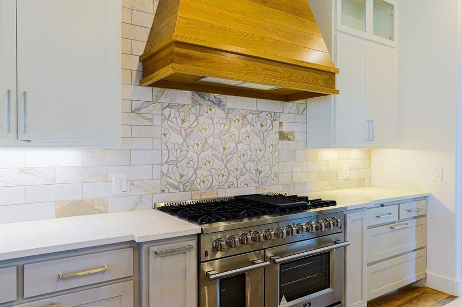 Kitchen with range with two ovens, backsplash, light stone countertops, hardwood / wood-style flooring, and custom range hood