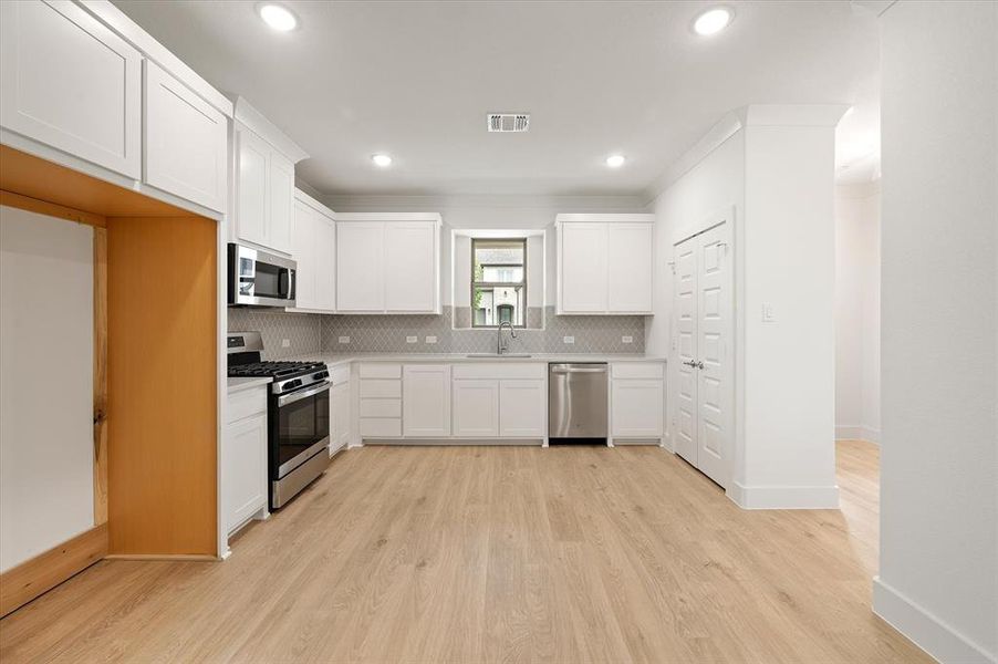 Kitchen featuring appliances with stainless steel finishes, sink, backsplash, light hardwood / wood-style floors, and white cabinetry