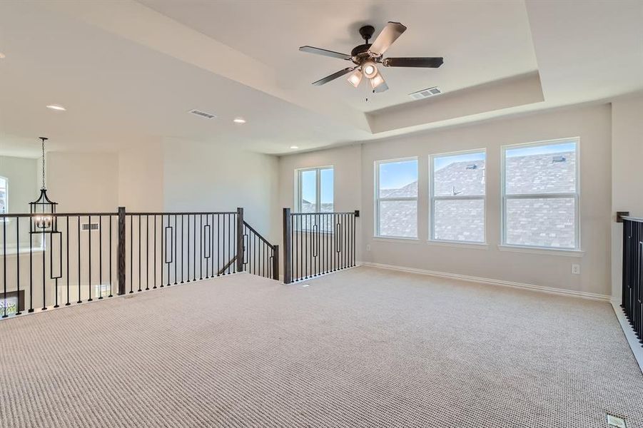 Empty room with a raised ceiling, carpet, and ceiling fan with notable chandelier