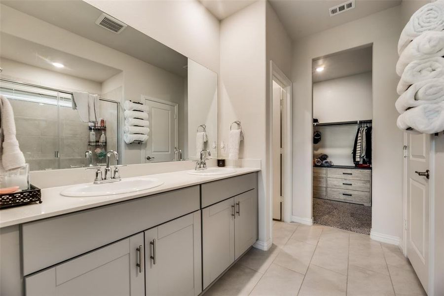Bathroom featuring tile floors, vanity with extensive cabinet space, a shower with shower door, and double sink