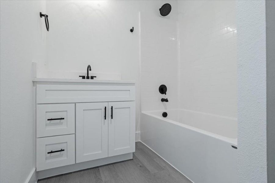 Bathroom featuring tiled shower / bath combo, vanity, and wood-type flooring