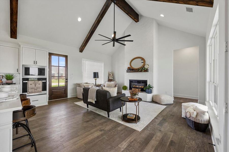 Living room featuring dark hardwood / wood-style floors, high vaulted ceiling, ceiling fan, a fireplace, and beamed ceiling