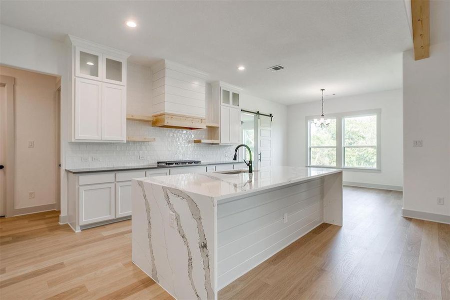 Kitchen featuring white cabinets, light hardwood / wood-style flooring, and an island with sink