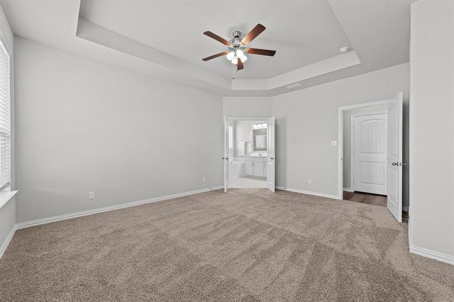 Unfurnished bedroom with a raised ceiling, connected bathroom, ceiling fan, and carpet floors