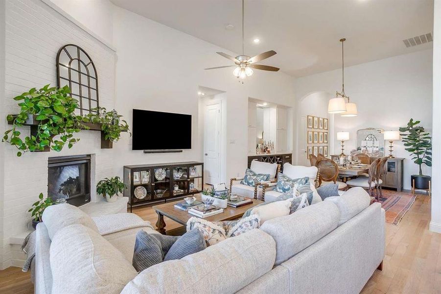 Living room featuring a fireplace, a high ceiling, light wood-type flooring, and ceiling fan