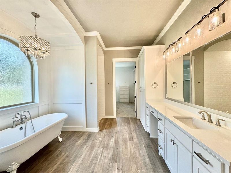 Primary Bathroom featuring hardwood / wood-style flooring, a chandelier, vanity, a bathtub, and ornamental molding