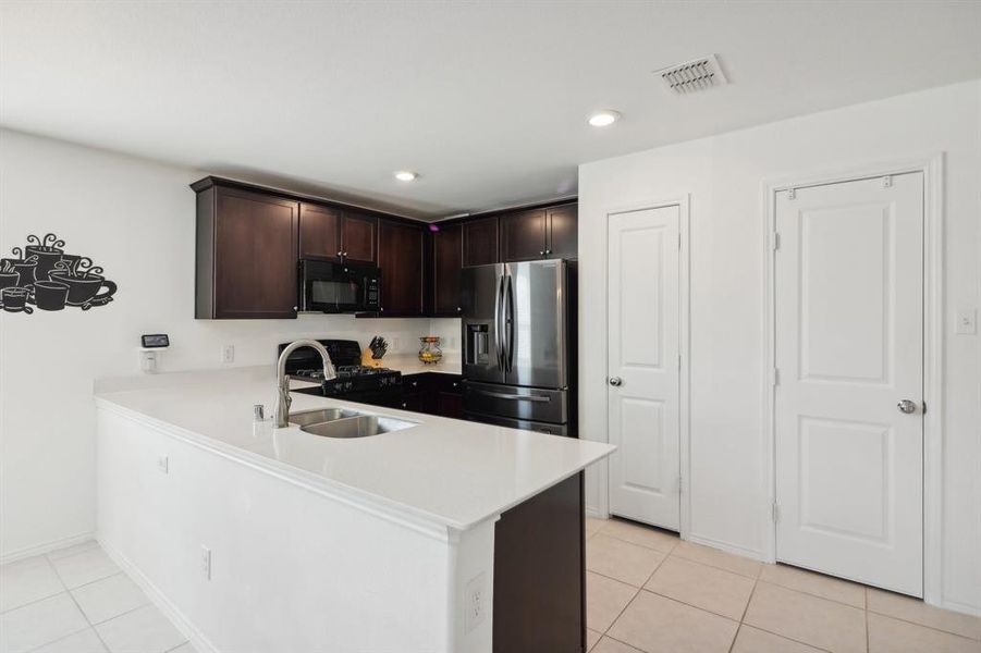 Kitchen with light tile patterned flooring, dark brown cabinets, sink, kitchen peninsula, and black appliances