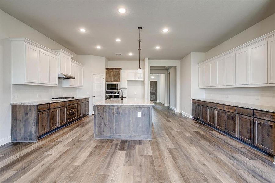 Kitchen featuring pendant lighting, light hardwood / wood-style floors, an island with sink, white cabinets, and appliances with stainless steel finishes