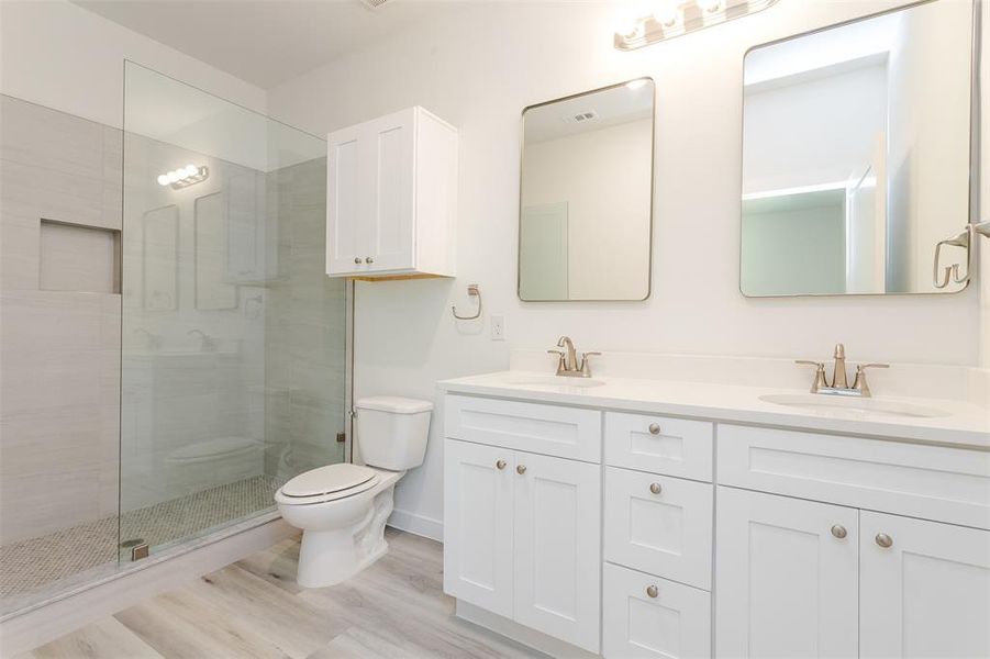 Bathroom with hardwood / wood-style floors, oversized vanity, double sink, a shower with door, and toilet