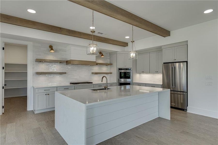 Kitchen featuring light hardwood / wood-style flooring, a center island with sink, hanging light fixtures, beam ceiling, and stainless steel appliances