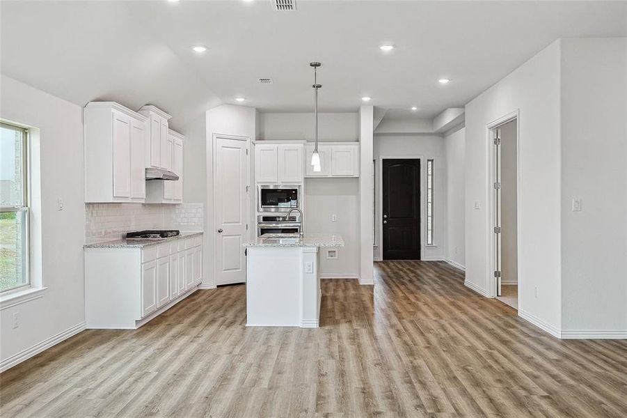 Kitchen with light hardwood / wood-style floors, light stone countertops, a center island with sink, and stainless steel appliances