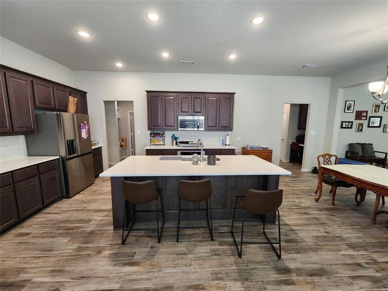 Kitchen featuring dark brown cabinetry, an island with sink, hardwood / wood-style flooring, stainless steel appliances, and a breakfast bar area