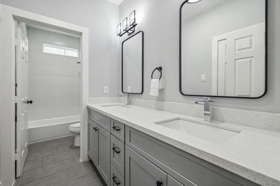 Guest bath with dual vanities, tub/ shower combo with tile surround.