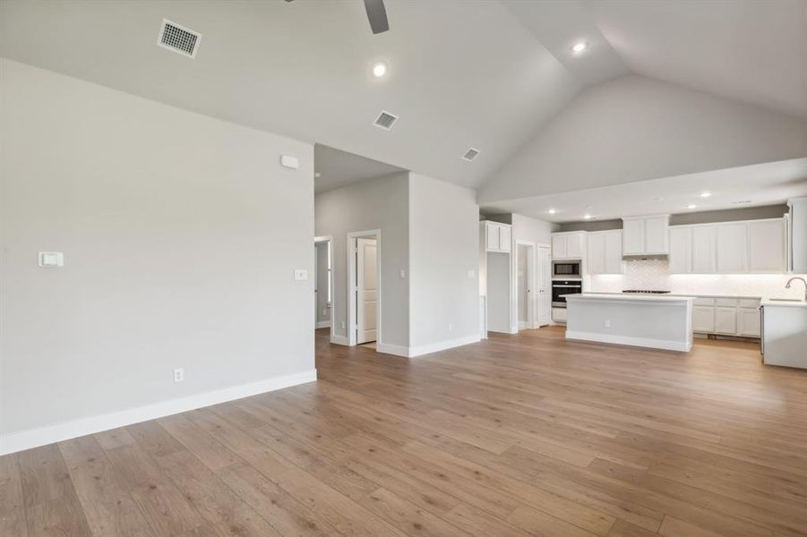 Unfurnished living room featuring high vaulted ceiling, light wood-type flooring, ceiling fan, and sink