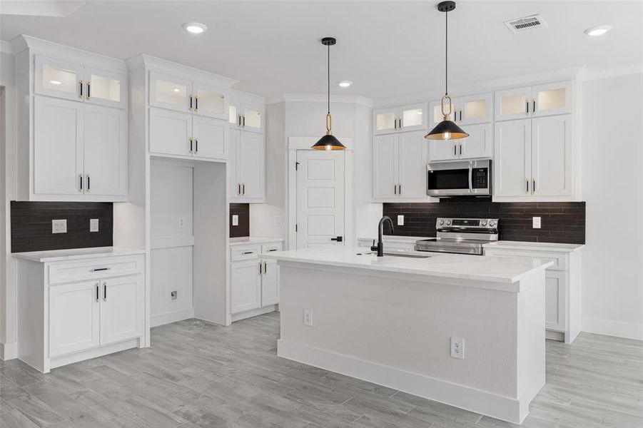 Kitchen featuring light wood-type flooring, appliances with stainless steel finishes, an island with sink, and sink