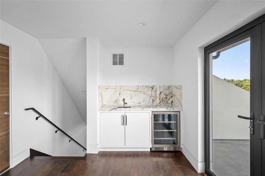 This elegant wet bar, conveniently located on the third floor and adjacent to the rooftop terrace, offers easy access for outdoor entertaining and features a sleek Sub-Zero beverage cooler complemented by a minimalist design with white cabinetry and modern hardware.