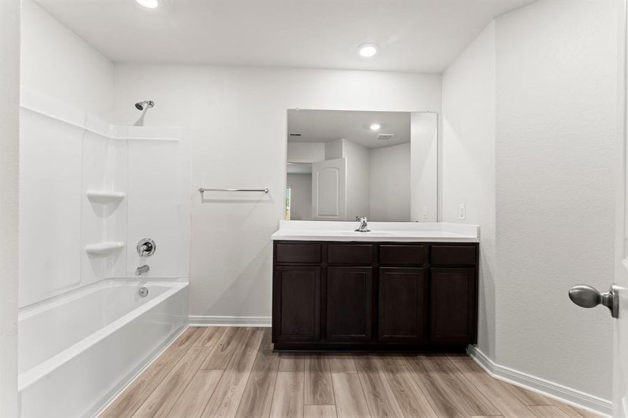 Your en-suite bath features  wood-look vinyl plank flooring, single vanity with extended solid surface counter top and integrated sink, toilet, and shower/tub combo with built-in shelving.