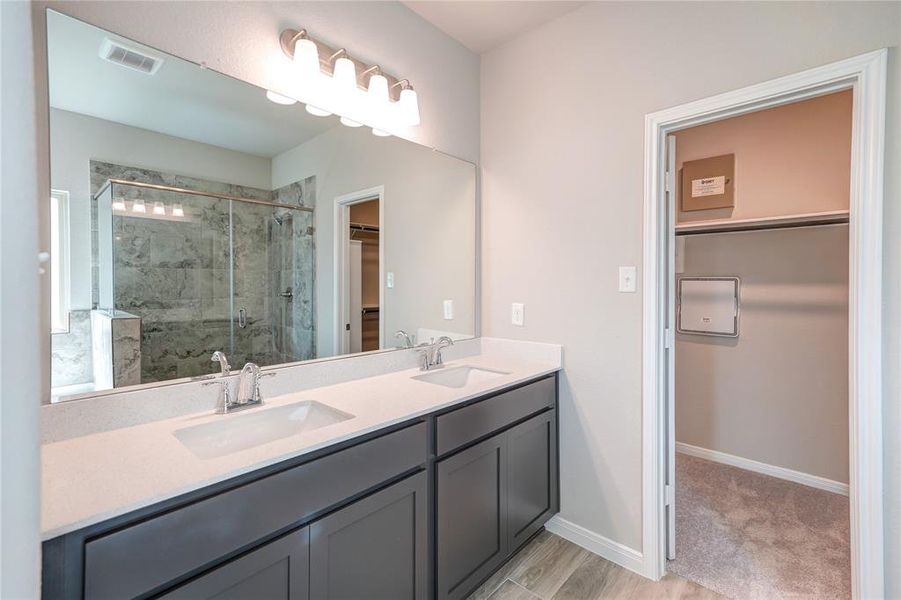 This modern bathroom features dual sinks with a large mirror, ample lighting, and a separate shower area visible through a glass door. It also includes a built-in closet for extra storage. The neutral walls and dark cabinetry create a sophisticated color scheme.