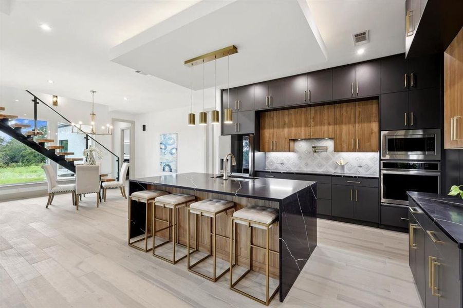 Kitchen featuring stainless steel appliances, sink, hanging light fixtures, decorative backsplash, and a kitchen island with sink