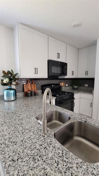 Kitchen featuring stove, light stone counters, backsplash, sink, and white cabinets