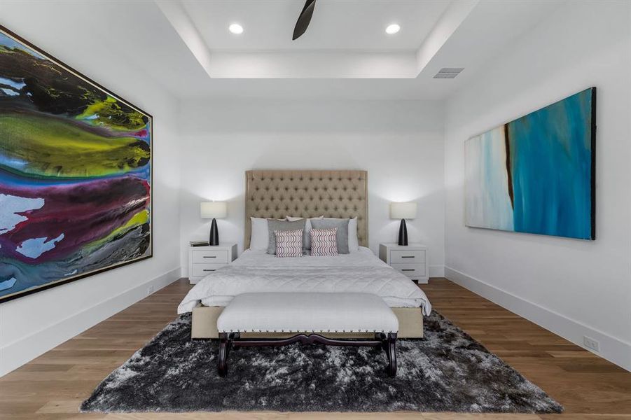 Bedroom with hardwood / wood-style floors, ceiling fan, and a raised ceiling