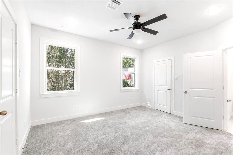 Primary bedroom with 2 windows, ceiling fan, and gray carpet.