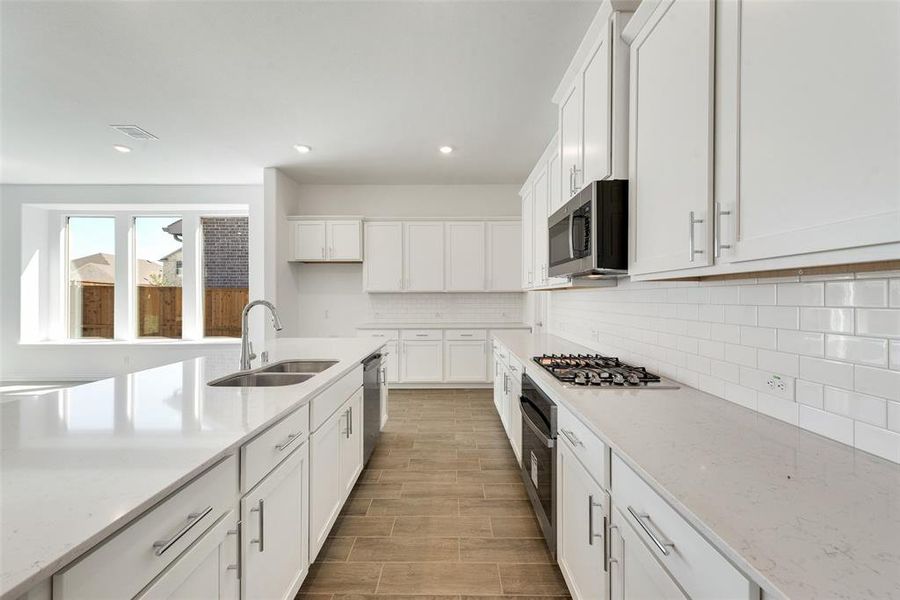 Kitchen featuring appliances with stainless steel finishes, light stone counters, white cabinets, light wood-type flooring, and sink