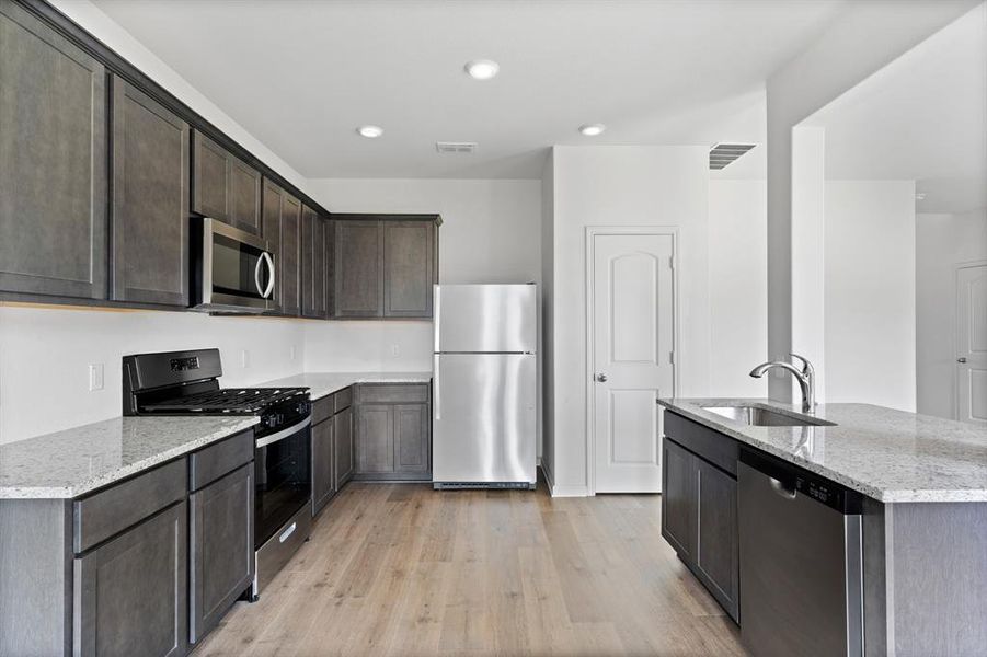 Kitchen featuring sink, light wood-style flooring, light stone counters, and stainless steel appliances