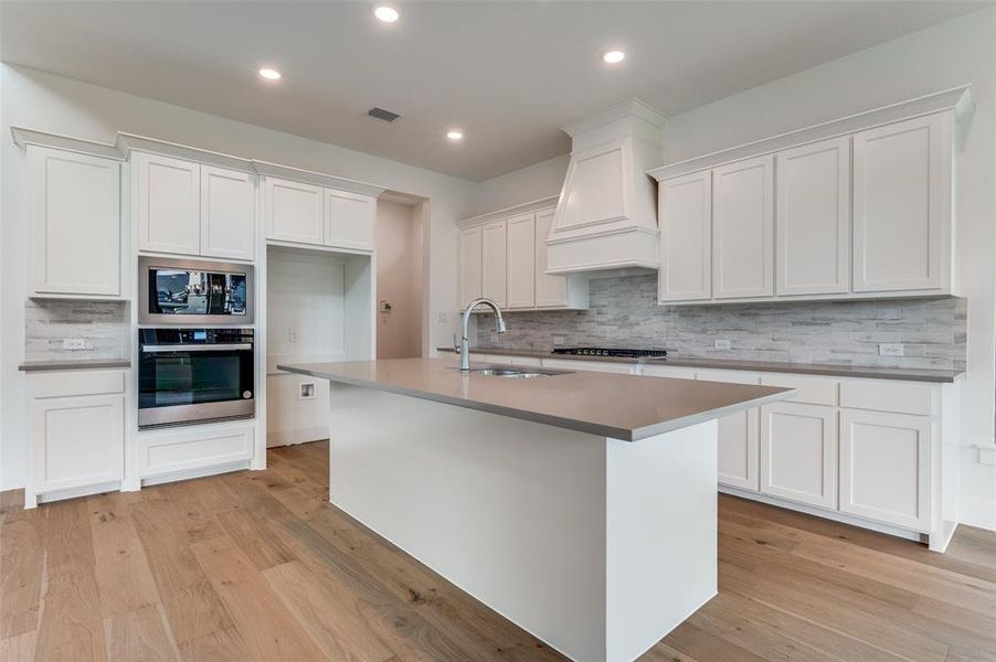 Kitchen featuring light hardwood / wood-style flooring, a center island with sink, sink, white cabinets, and appliances with stainless steel finishes