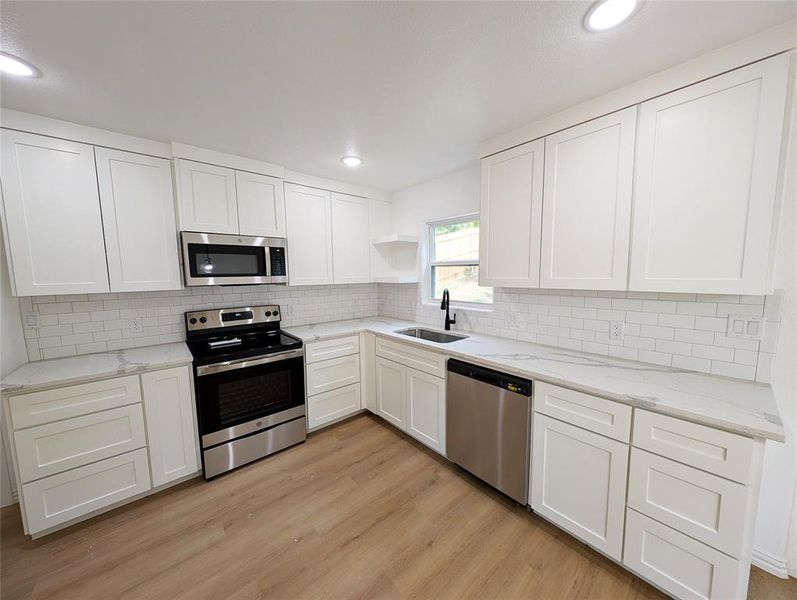 Kitchen with appliances with stainless steel finishes, white cabinetry, light stone countertops, light hardwood / wood-style flooring, and sink