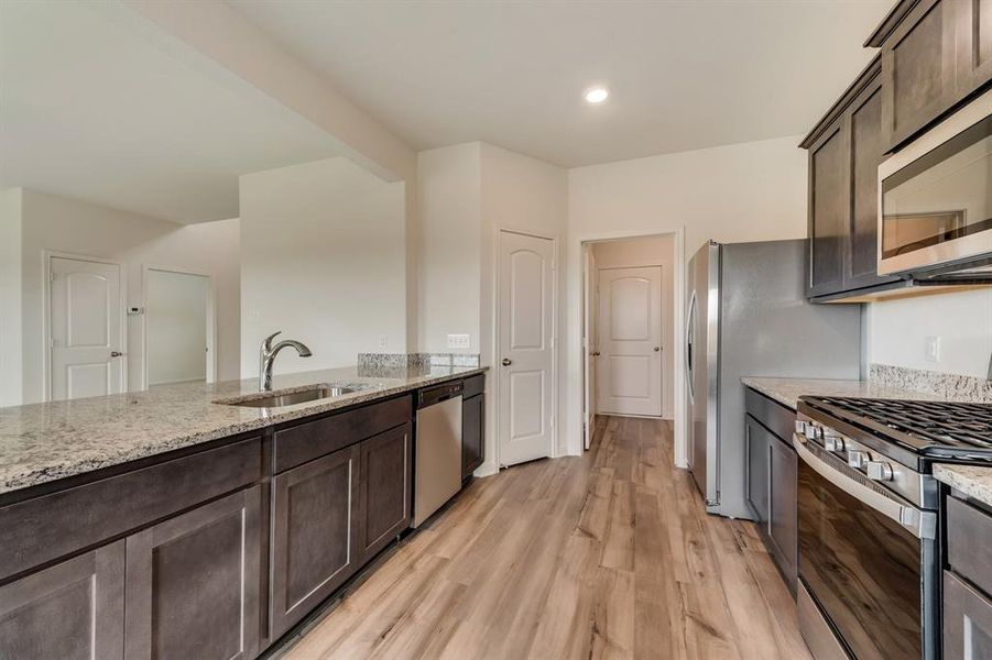 Kitchen featuring appliances with stainless steel finishes, light hardwood / wood-style flooring, dark brown cabinetry, sink, and light stone counters