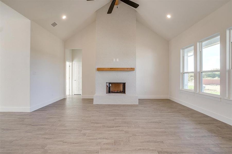 Unfurnished living room with ceiling fan, high vaulted ceiling, light wood-type flooring, and a fireplace