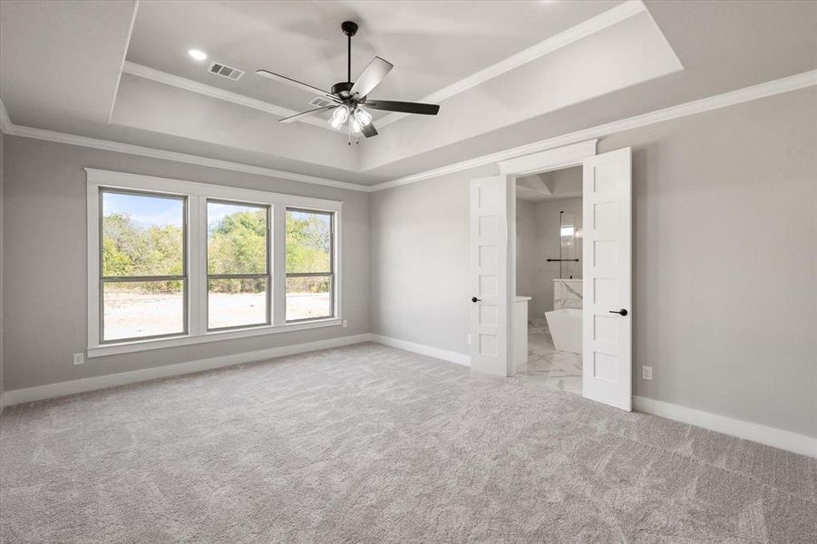 Unfurnished bedroom featuring a tray ceiling, ceiling fan, light carpet, connected bathroom, and crown molding