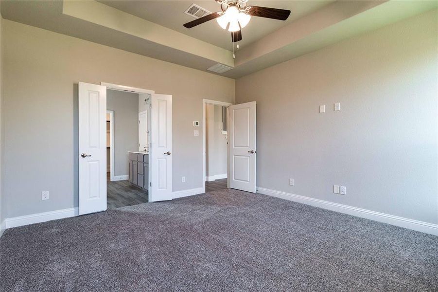 Unfurnished bedroom featuring dark colored carpet, ceiling fan, a tray ceiling, and connected bathroom