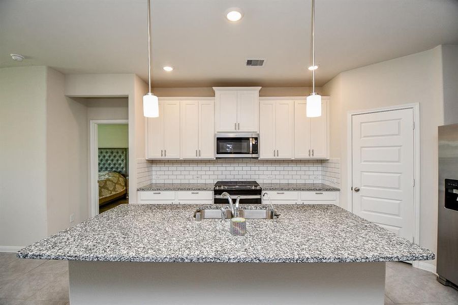 Modern kitchen with granite countertops, white cabinetry, subway tile backsplash, and stainless steel appliances.