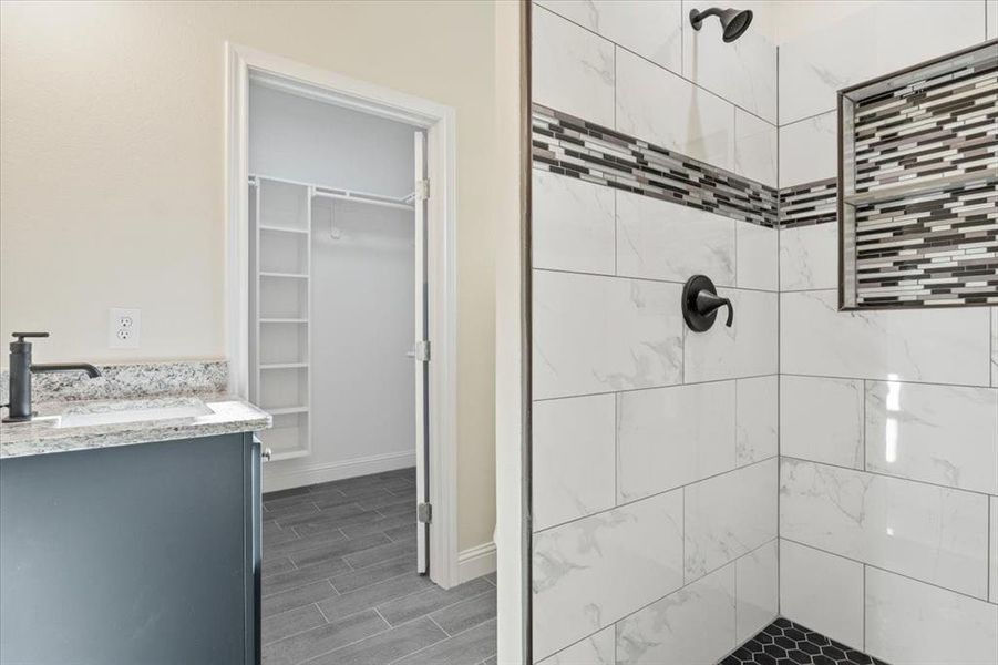 Bathroom featuring a tile shower, tile flooring, and vanity